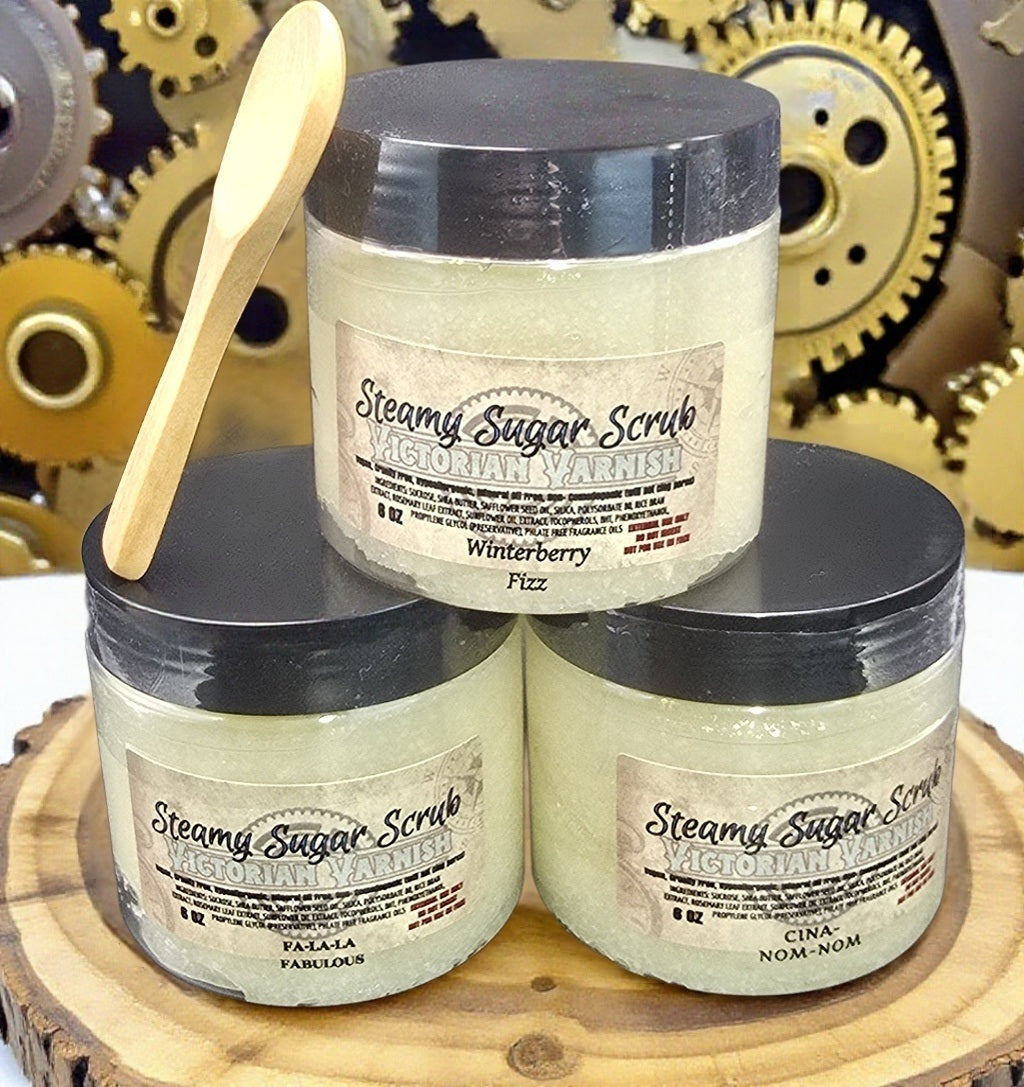 Three jars of 'Steamy Sugar Scrub' with a wooden spoon on a wooden surface and gear background.