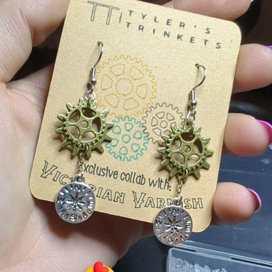We will be offering earrings this month! In an Exclusive Collab with Tyler’s Trinkets!  Gears for Ears    $16 only 20 Available  Description : Silver-toned nickel-free compass charms suspended below a set of antique bronze finish gears on hypoallergenic stainless steel ear-wire hooks. (Gear charms may vary slightly) Drop length 42mm (62mm including hook)