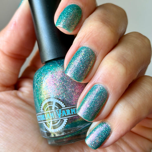 Hand with teal glittery nail polish holding a bottle of the same polish.
